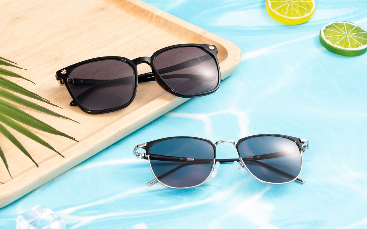 Two pairs of sunglasses resting on a wooden board — one dark frame, one metal half-frame