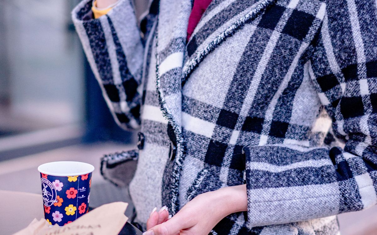 A woman in a plaid coat holding a paper cup